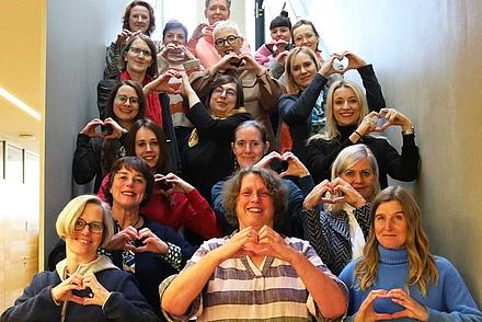 Frauen auf einer Treppe im DHBW Gebäude formen mit der Hand ein Herz