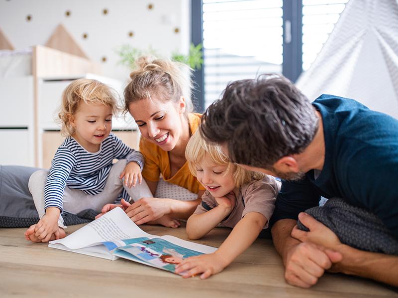 Das Foto zeigt einen Mann, eine Frau und zwei Kinder, die zusammen durch ein Kinderbuch blättern.