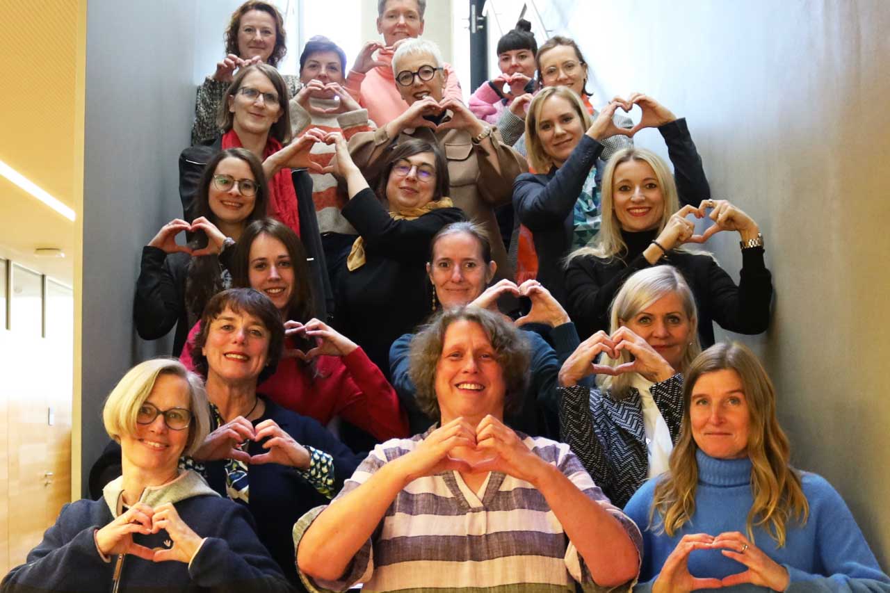 Frauen auf einer Treppe im DHBW Gebäude formen mit der Hand ein Herz