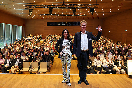 Auf diesem Bild winkt die Rektorin Nicole Graf und der Prorektor Tomás Bayón in die Kamera. Im Hintergrund der Bühne winken die neuen Studierenden und die Studiengangs-Teams.