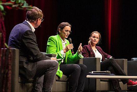 Auf dem Bild sind drei Personen bei einer Podiumsdiskussion zu sehen.