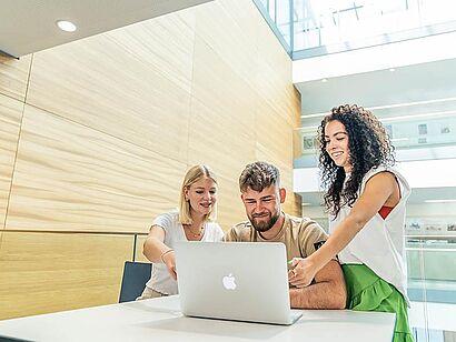 Auf dem Foto sind drei Studierende zu sehen, die gemeinsam auf einen Laptop schauen.
