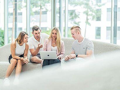 Auf dem Foto sind vier Studierende zu sehen, die gemeinsam auf einen Laptop schauen.