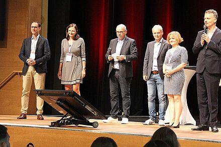 Begrüßung bei den Retail Innovation Days 2022. Auf der Bühne stehen von links nach rechts: Prof. Dr. Oliver Janz, Prof. Dr. Daniela Wiehenbrauk, Prof. Dr. Stephen Rüschen, Prof. Dr. Carsten Kortum, Prof. Dr. Beate Scheubrein und Prof. Dr. Thomás Bayón.