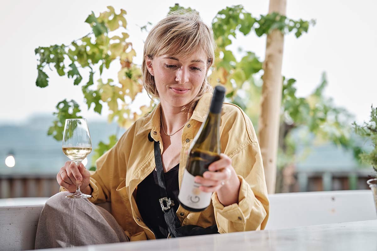 Frau hält ein Weinglas und  eine Weinflasche und sitzt am Tisch