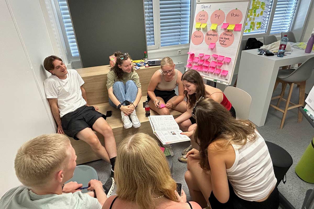 eine Gruppe Studierender sitzt um ein Flip Chart und diskutiert