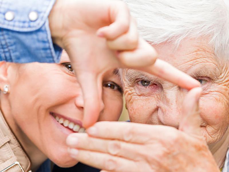 Das Foto zeigt eine jüngere und eine ältere Person, die mit ihren Händen einen Rahmen formen.