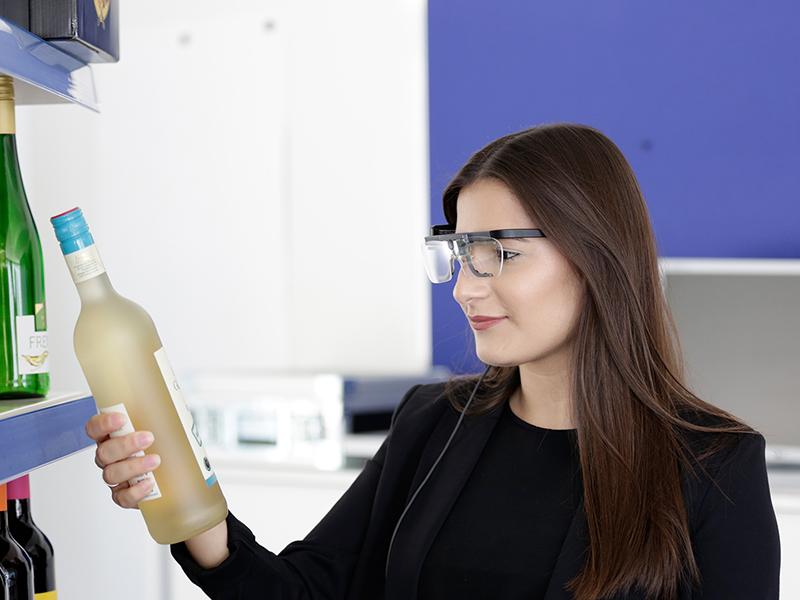 Das Foto zeigt eine Frau, die eine Eyetracking-Brille trägt und eine Weinflasche in der Hand hat.