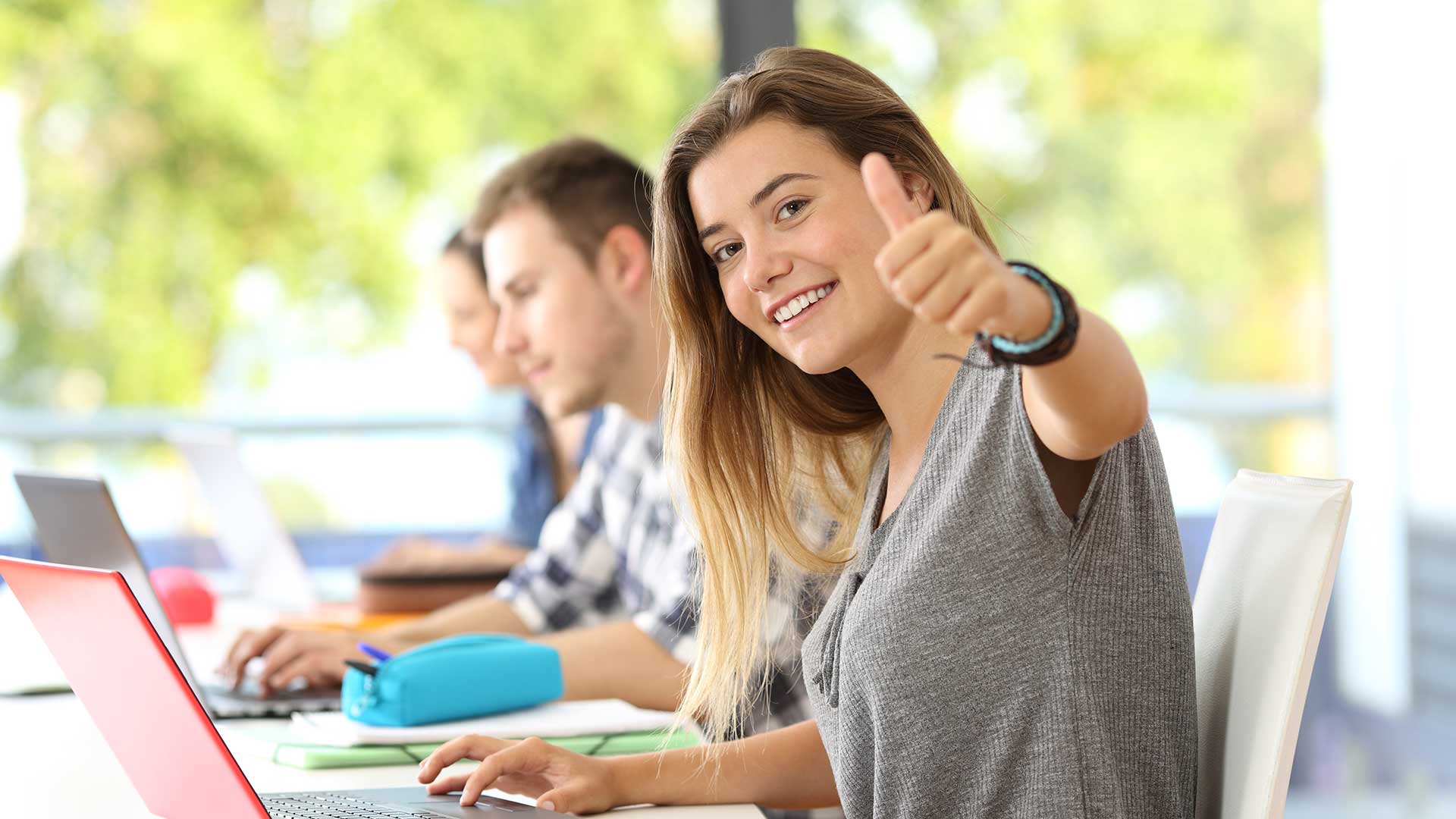 Remind Eine Studentin sitzt am Laptop und zeigt den Daumen nach oben