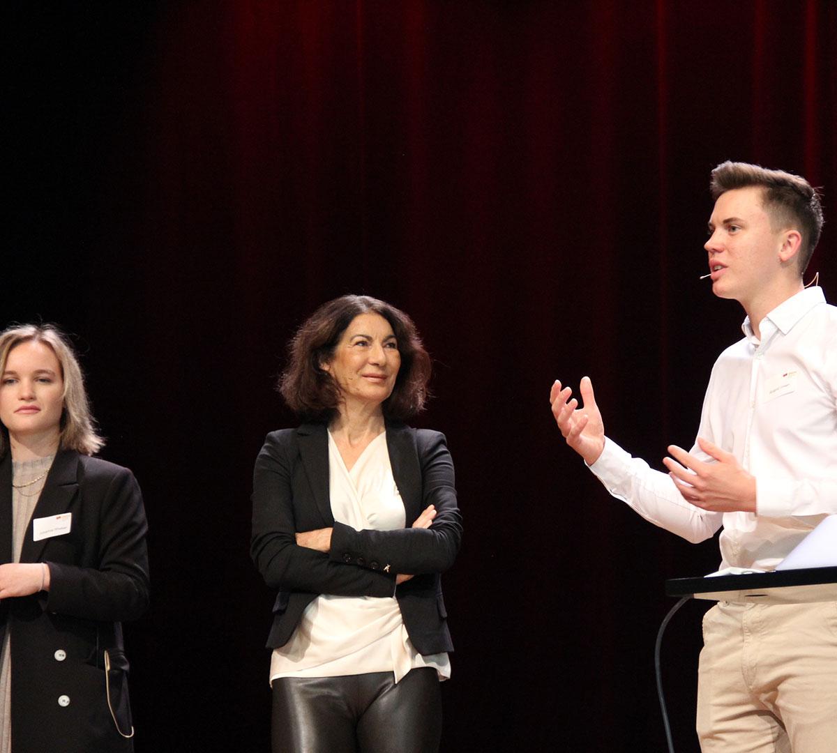 Zwei Frauen und ein Mann informieren auf der Bühne der Aula am Bildungscampus über die Vorteile des dualen Studiums. 