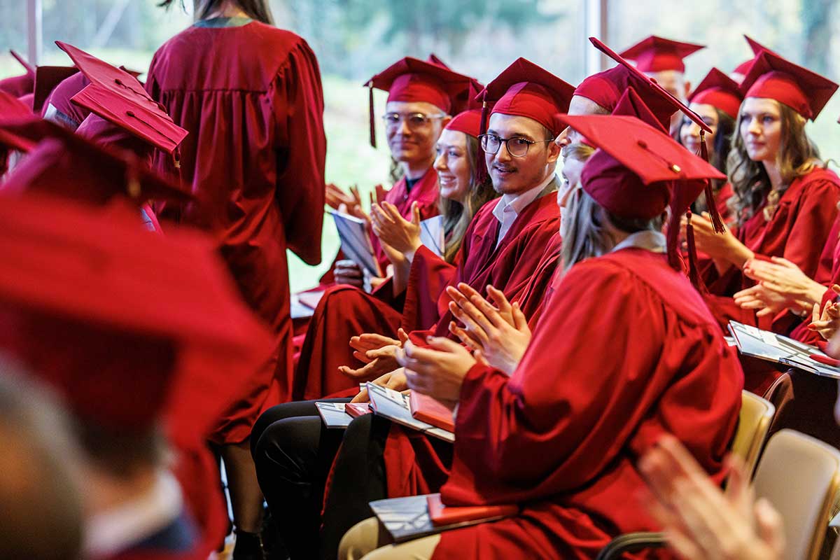 Absolventen mit roten Baretten und Talaren sitzen in den Reihen. 