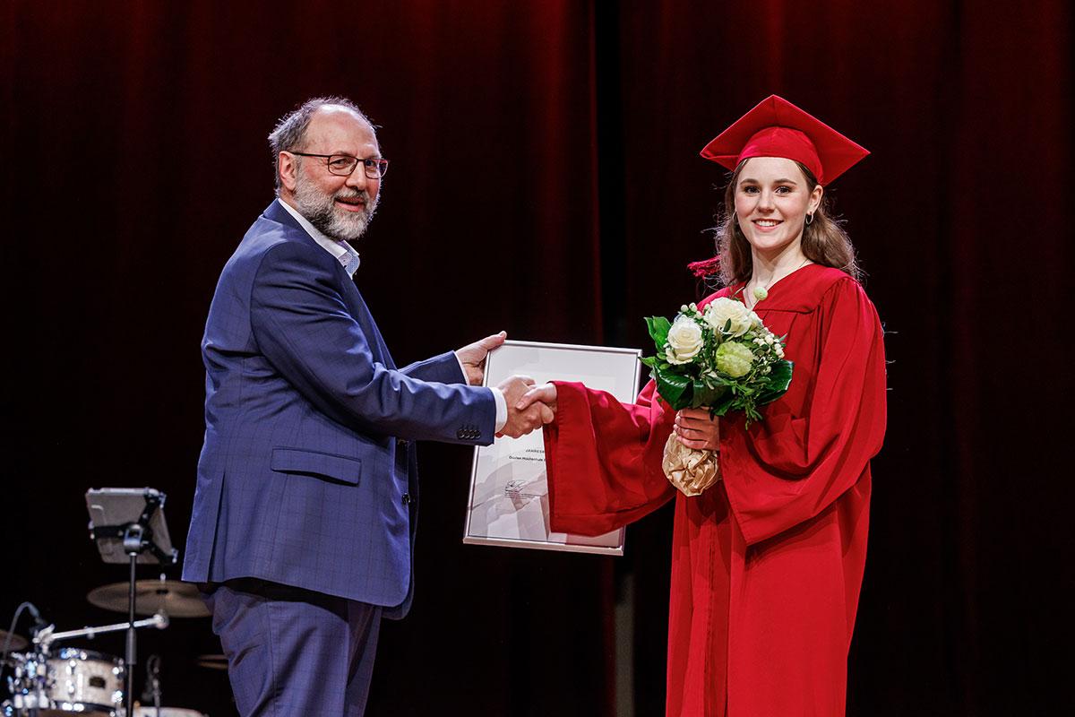 Wolfgang Jung überreicht Antonia Charlotte Rinsche eine Urkunde, sie hält einen Blumenstrauß in der Hand. 