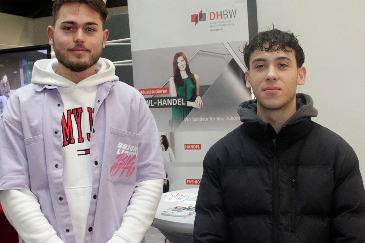 Zwei junge Männer stehen vor einem Roll-up vom Studiengang Handel. 