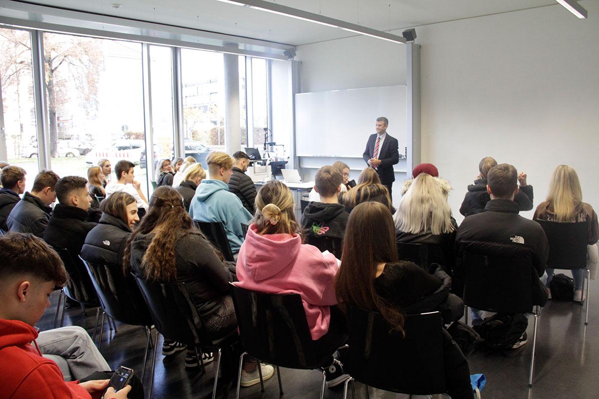 Professor steht im Hintergrund vor vollbesetztem Vorlesungsraum. 