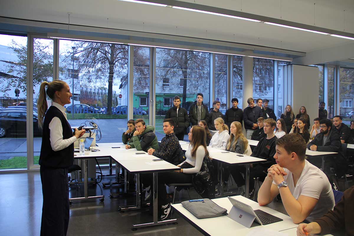 Schüler*innen sitzen in einem voll gepackten Vorlesungsraum, vorne steht unsere Studienberaterin Katja Eickert. 