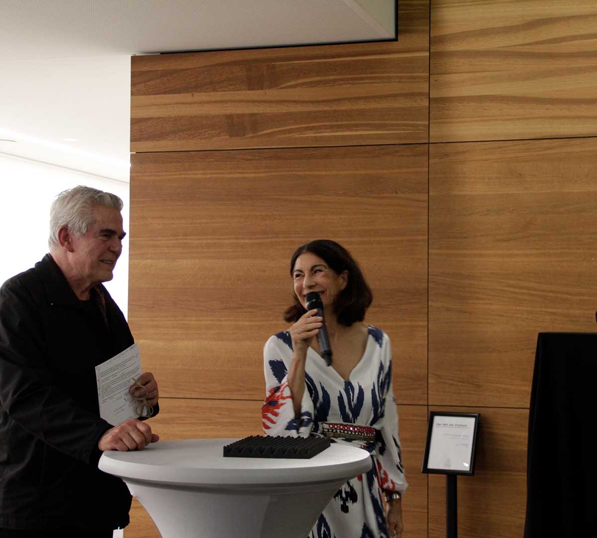 Der Künstler Malte Wiethüchter und die Rektorin Prof. Dr. Nicole Graf stehen am Podium und sprechen zum Publikum.