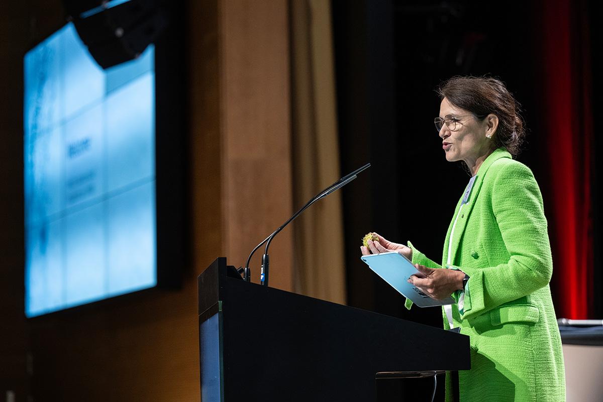Die Präsidentin der DHBW Prof. Dr. Martina Klärle steht vor einem Rednerpult, im Hintergrund eine erleuchtete Leinwand. Frau Klärle trägt einen neongrünen Blazer und gestikuliert beim Sprechen mit den Händen. 
