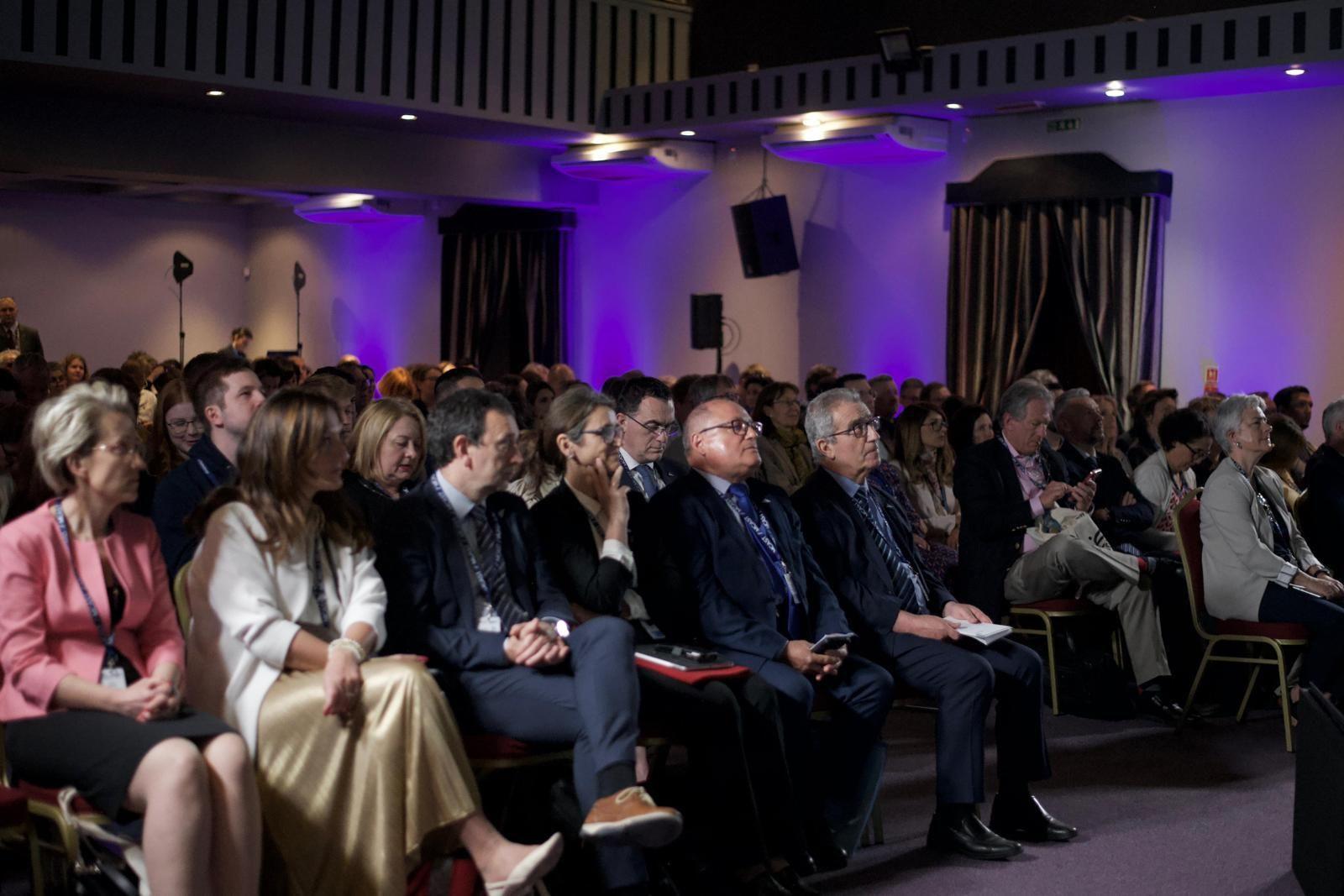 Die Teilnehmer der Konferenz sitzen in einem abgedunkelten Saal mit lila Lichteffekten und hören zu. Durch zahlreiche hochkarätige Speaker aus Politik und Bildungswesen sowie Workshops und Informationsräume wurde eine eindrucksvolle Plattform für visionäre Diskussionen und praktische Lösungen geschaffen.