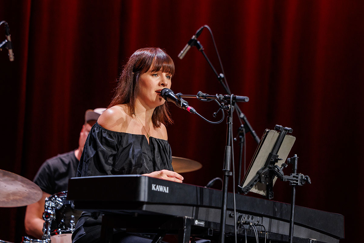 Die Band ROMY begleitete die drei Graduierungsfeiern den gesamten Tag über mit Pop- und Soulklassikern. Im Vordergrund sieht man die Sängerin am Keyboard in einem schulterfreien schwarzen Oberteil, während sie singt und Klavier spielt. 