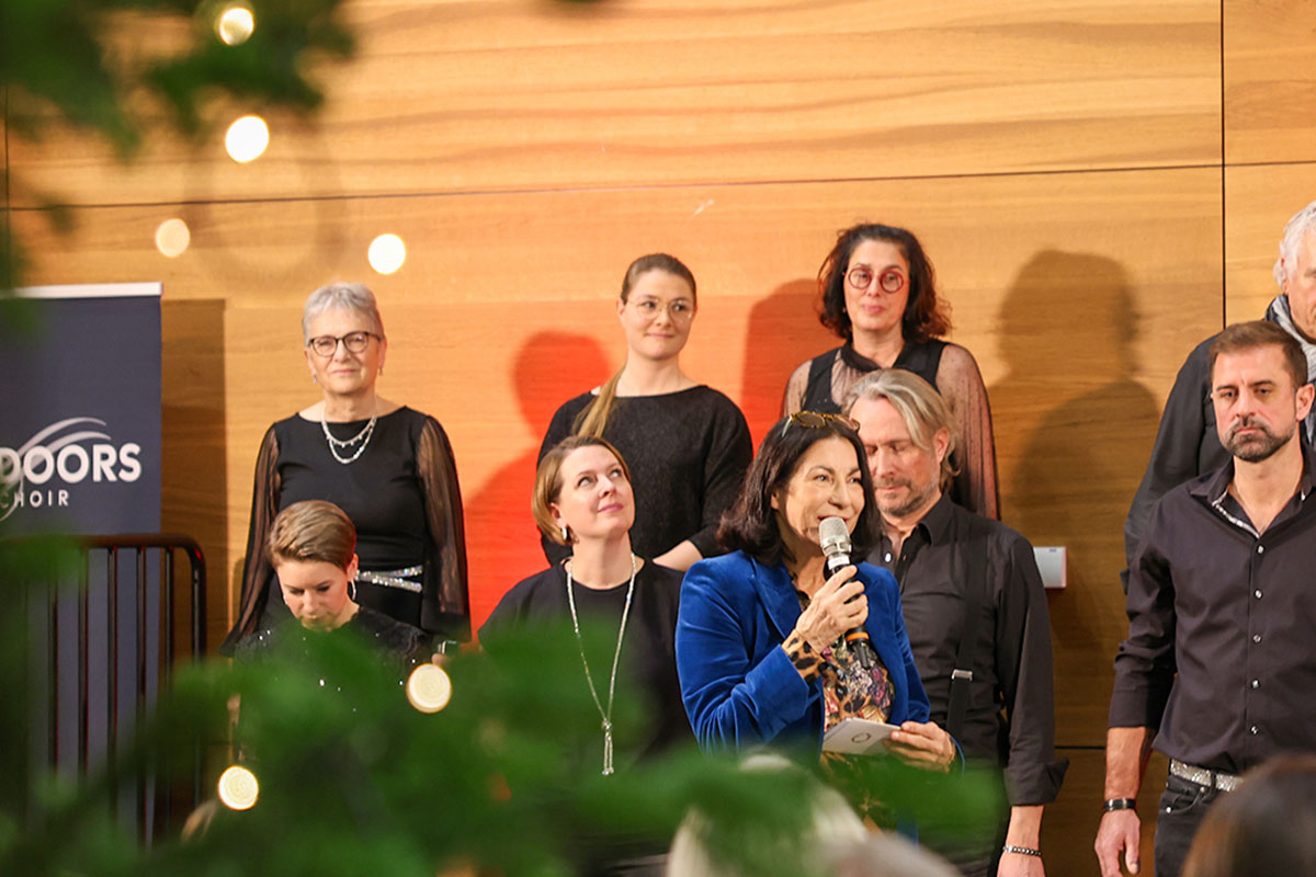 Rektorin Prof. Dr. Nicole Graf steht vor dem Chor in einem blauen Ensemble und begrüßt die Gäste. 