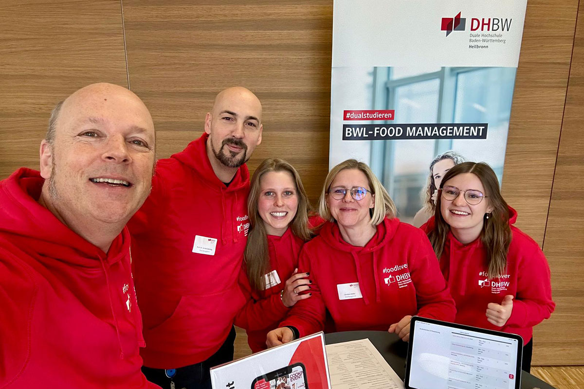 Das Team "Foodlovers" des Studiengang BWL-Food Management im Beratungseinsatz. Fünf Menschen im roten Hoodie mit weißer Aufschrift Foodlovers blicken in die Kamera. 