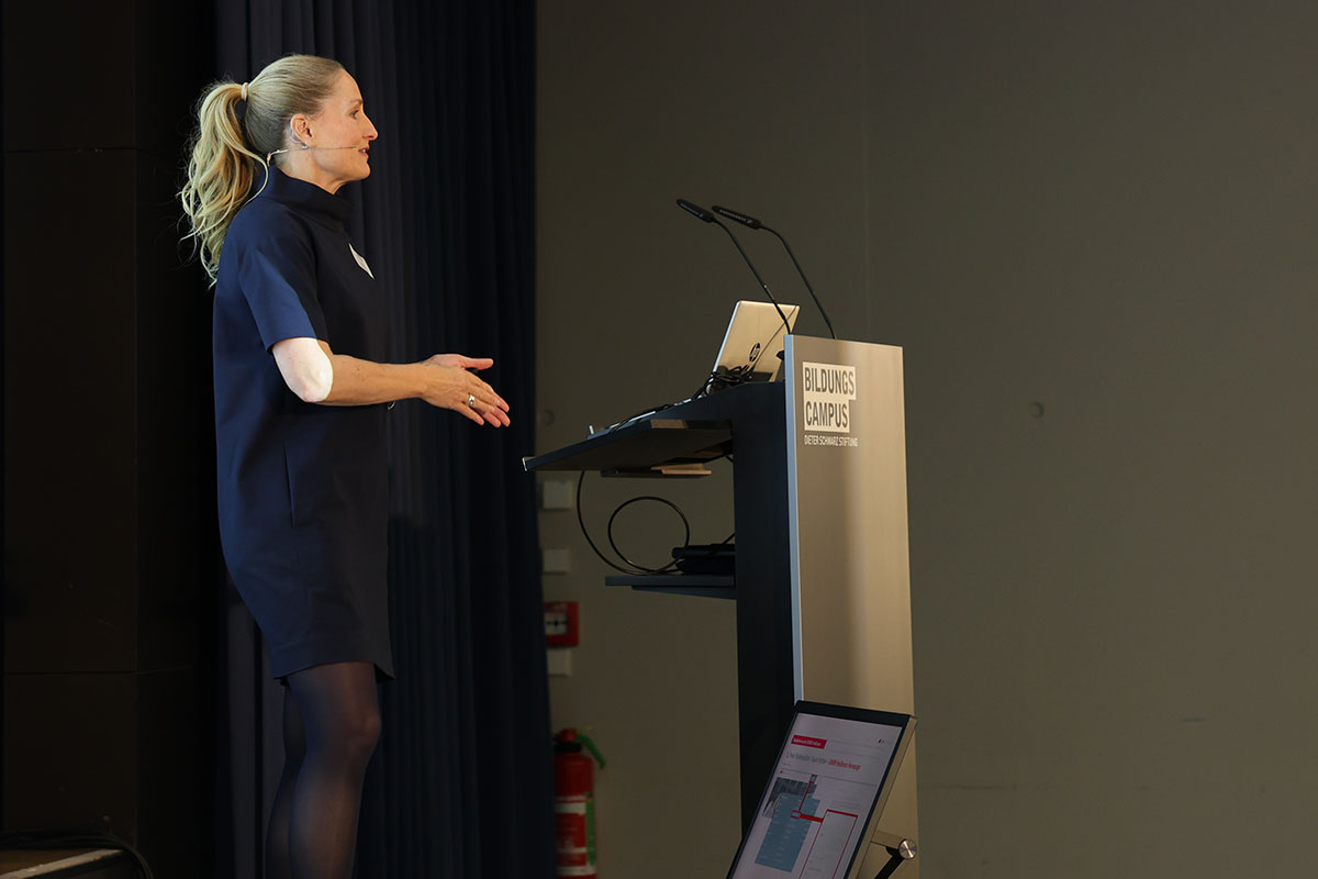 Studienberaterin Katja Eickert führt durch das Duale Studium - von der Bewerbung bis zum Bachelor-Abschluss. Ein Frau mit einem langen blonden Pferdeschwanz und blauem Kleid steht auf der Bühne und spricht. 