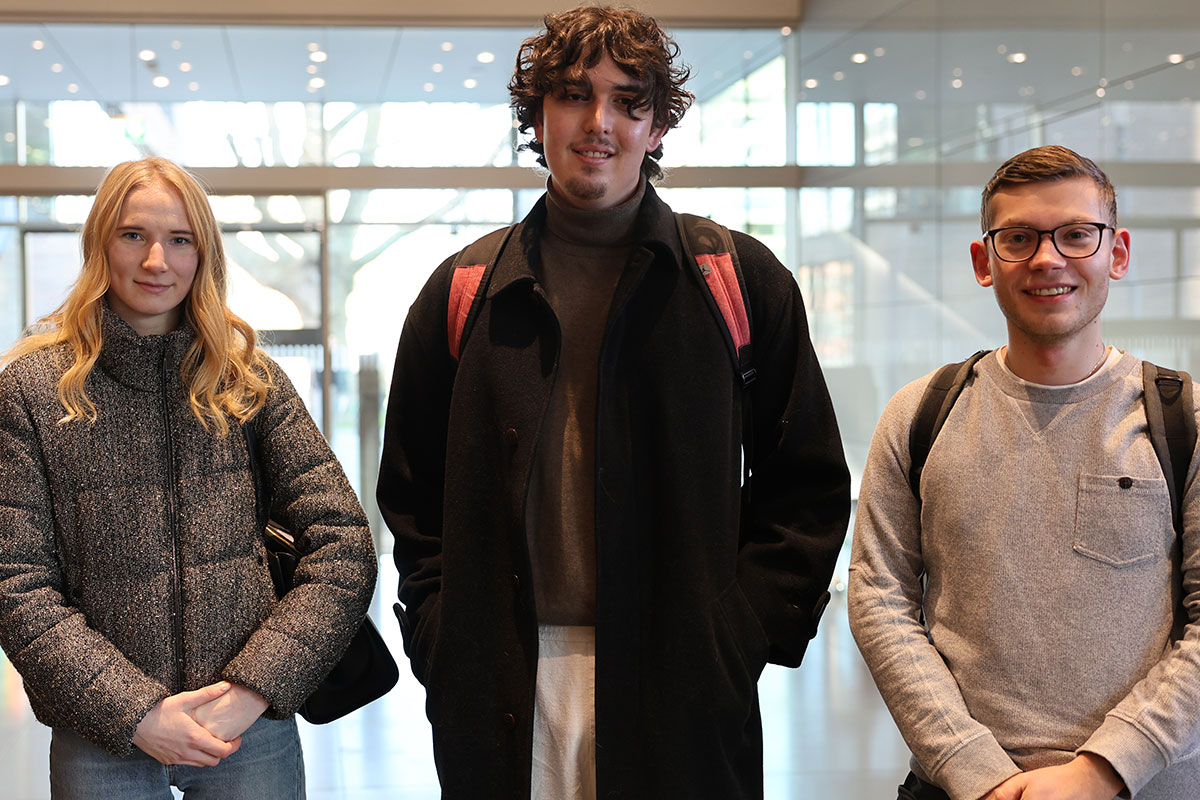 Die drei Studierenden von links nach rechts: Emma Hahn, Mihailo Vasovic und Maximilian Schock stehen im Foyer der Aula. 