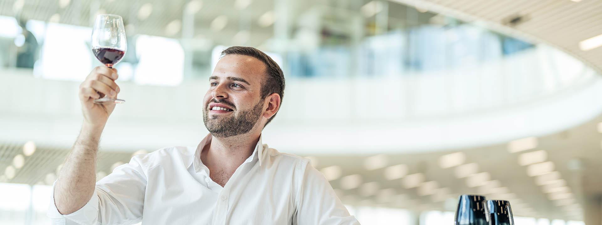 Auf dem Foto ist ein Mann zu sehen, der ein Glas Wein in der Hand hält und begutachtet.
