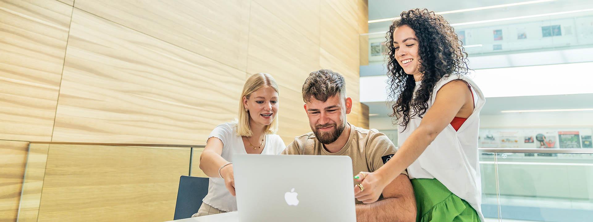 Auf dem Foto sind drei Studierende zu sehen, die zusammen in einen Laptop schauen.
